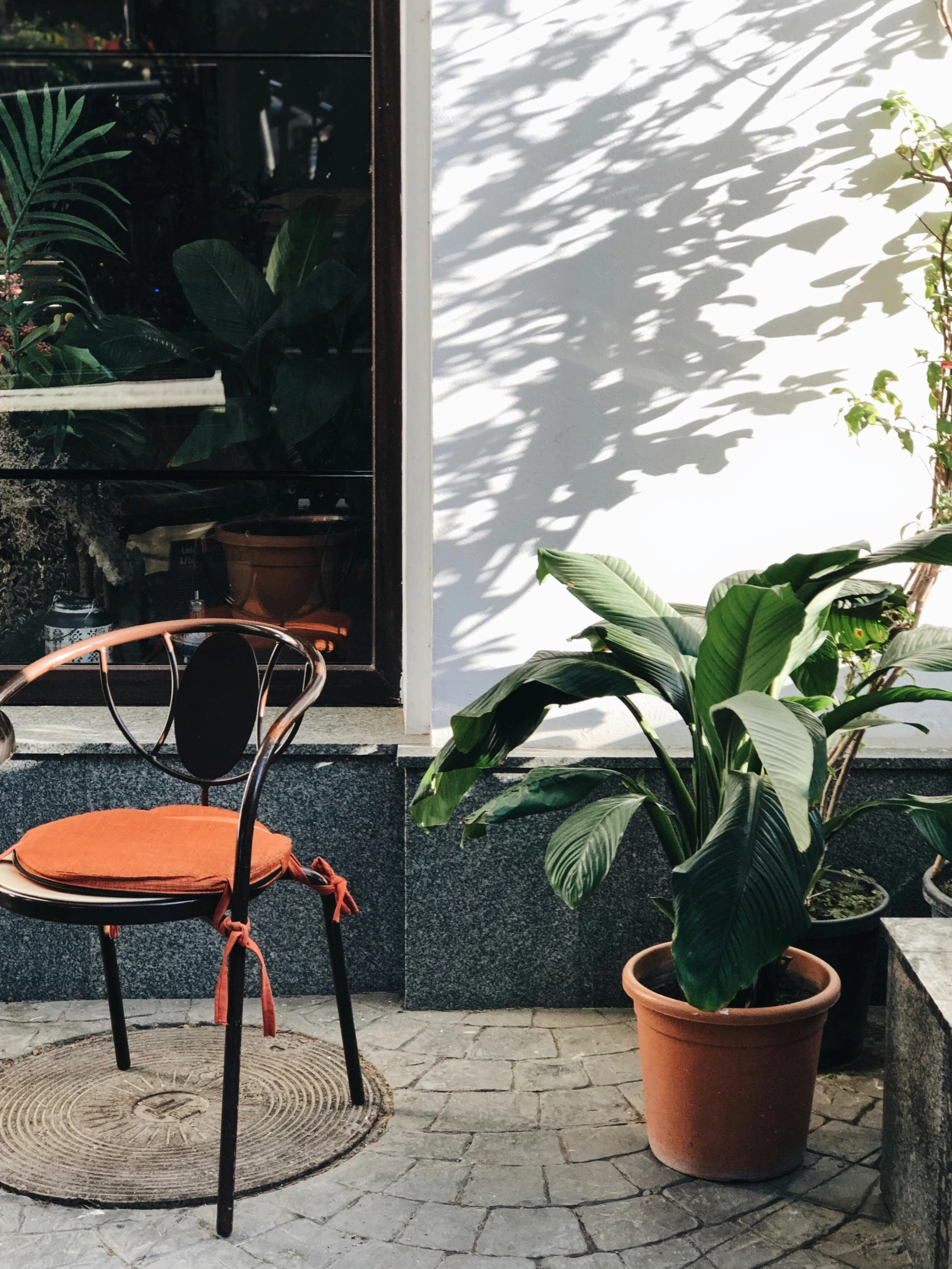 a chair sitting in front of a window next to a potted plant, by Anna Haifisch, trending on unsplash, brutalist courtyard, orange and black, profile image, jakarta