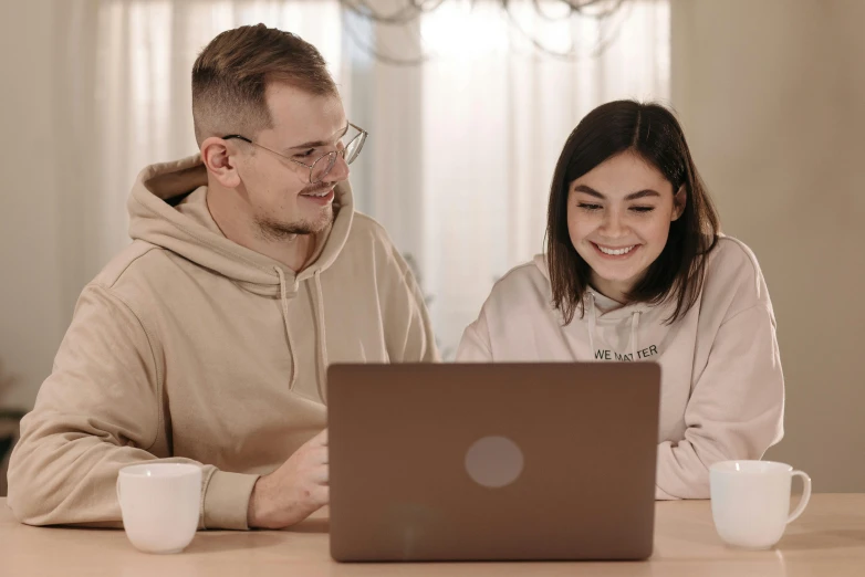 a man and a woman sitting at a table looking at a laptop, trending on pexels, brown, background image, educational, slight nerdy smile