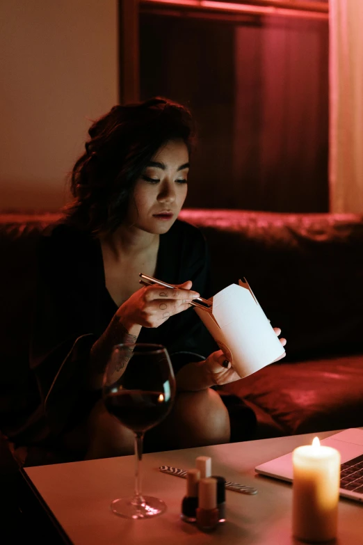 a woman sitting on a couch in front of a laptop, inspired by Nan Goldin, pexels contest winner, holding a candle holder, fine dining, a young asian woman, holding a bottle of arak