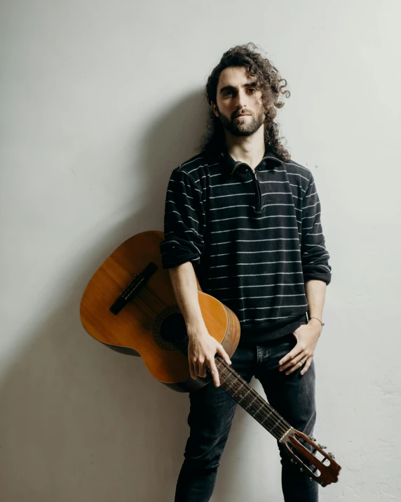 a man standing next to a wall with an acoustic guitar