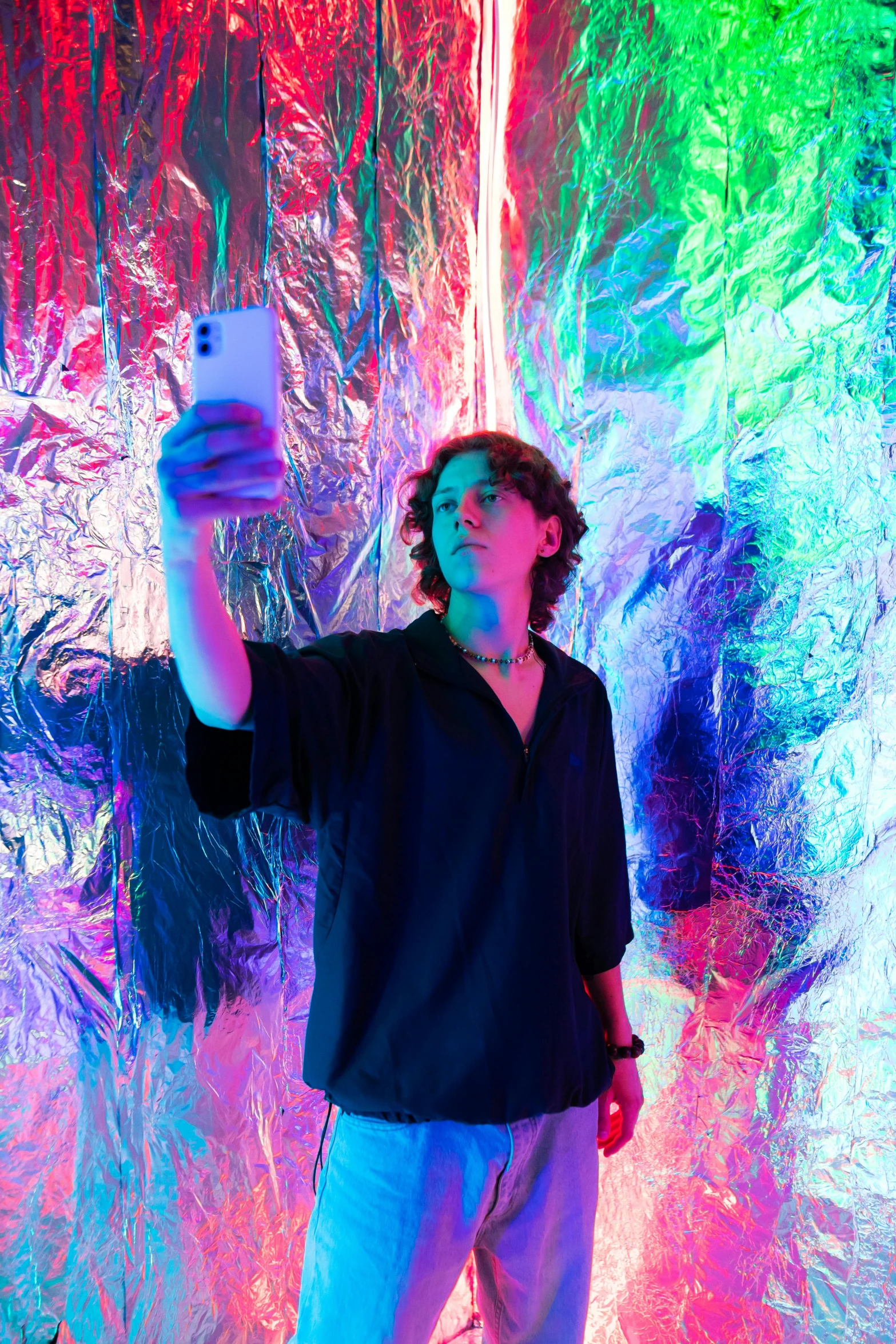 a man taking a picture of himself with a cell phone, an album cover, by Cafer Bater, trending on pexels, interactive art, iridescent neon, timothee chalamet, model posing, neo-expressionist