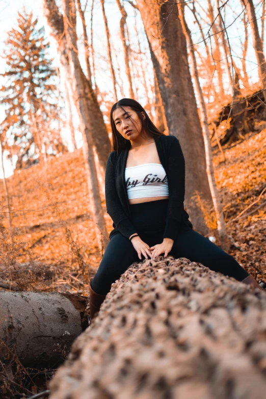 a woman sitting on a log in the woods, inspired by Elsa Bleda, unsplash, wearing a cropped tops, asian women, avatar image, low quality photo