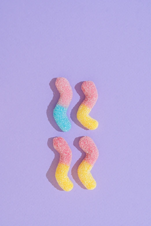 a couple of gummy worms sitting on top of a purple surface, inspired by Ren Hang, trending on pexels, candy pastel, bumps, detailed product image, woman is curved