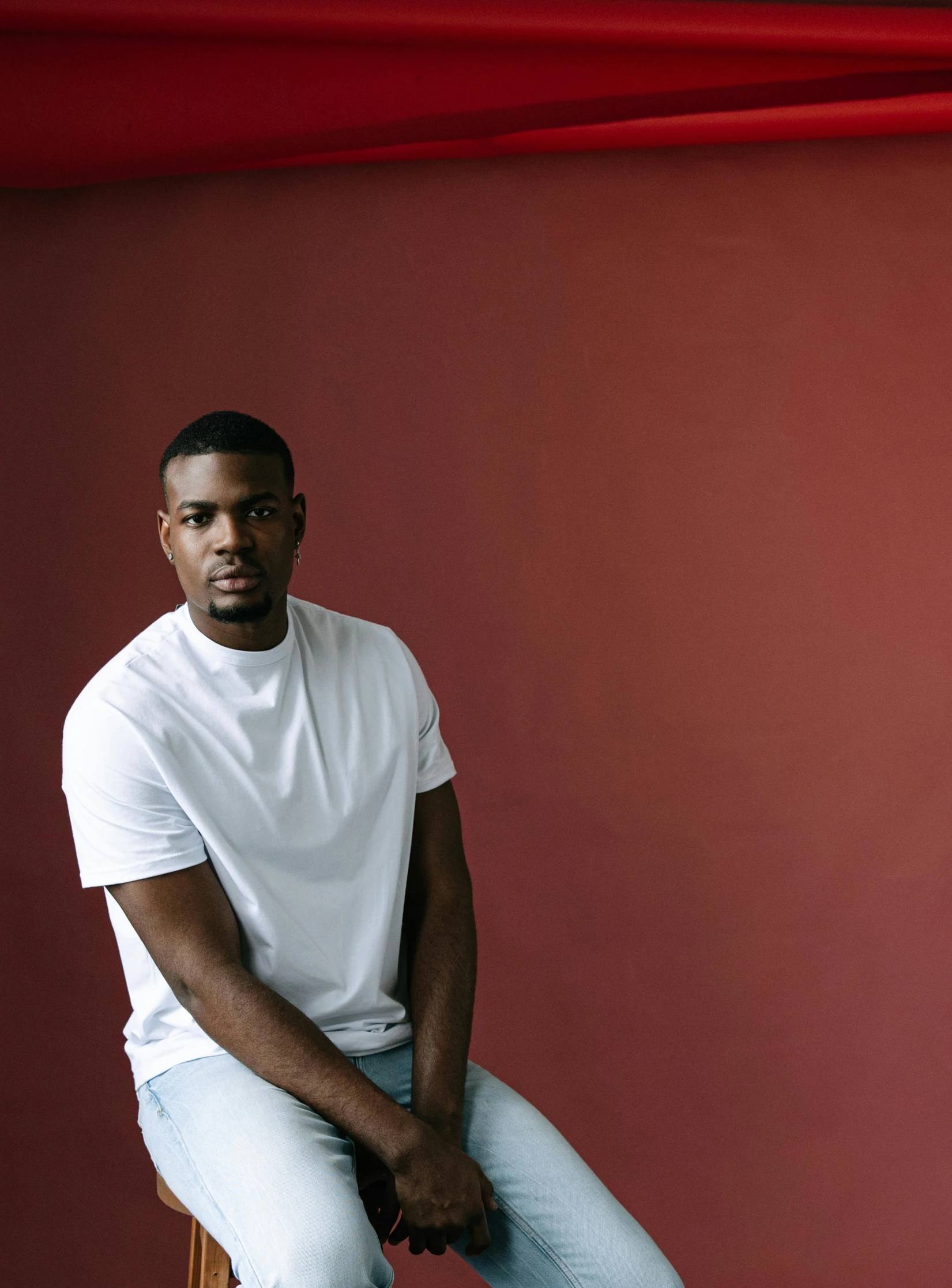 a man in a white shirt sitting against a red wall