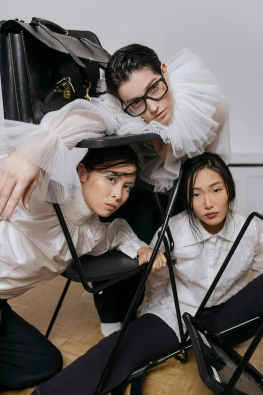 a group of people sitting on top of a wooden floor, wearing a white blouse, rei kawakubo artwork, with square glasses, sitting on a stool