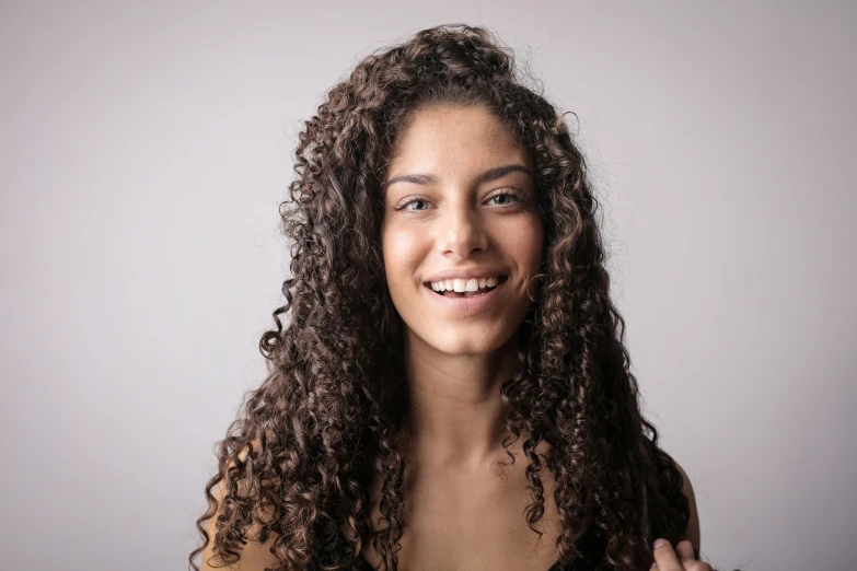 a woman with curly hair smiling at the camera, pexels contest winner, on grey background, mixed styles, brown, nika maisuradze