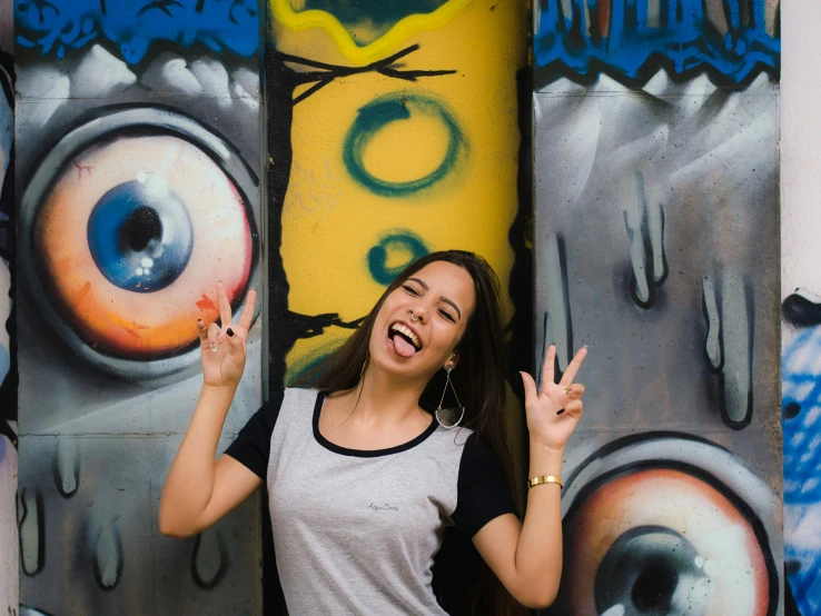 a woman standing in front of a wall covered in graffiti, pexels contest winner, round teeth and goofy face, avatar image, pose(arms up + happy), two eye art