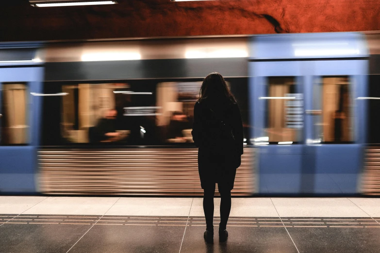 a person standing in front of a train, happening, metro, black and terracotta, shes alone, lit from behind