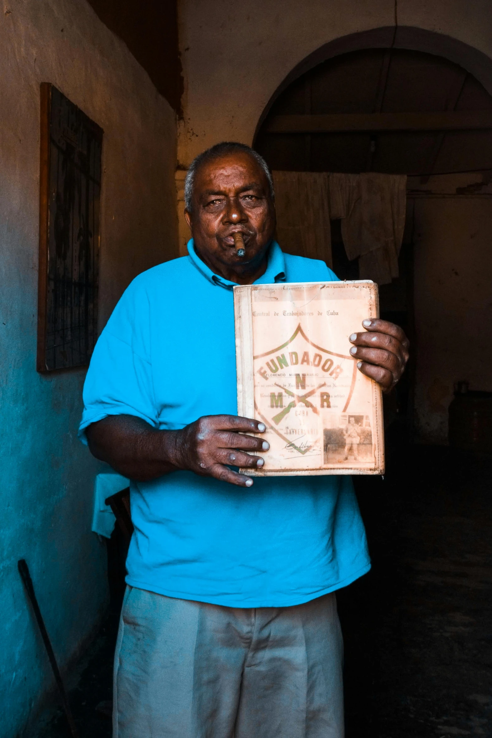 a man in a blue shirt holding a box, an album cover, pexels contest winner, somalia, with cigar, very old, he is holding a large book