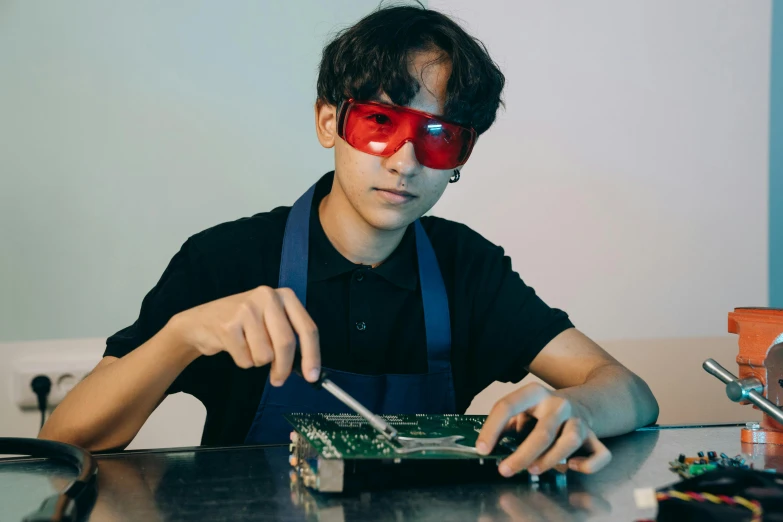 a young man sitting at a table working on a computer, an album cover, inspired by Yasutomo Oka, pexels contest winner, motherboard circuitry, wearing 3 d glasses, maintenance photo, school class