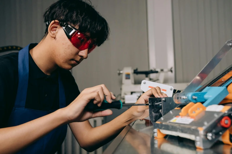 a man working on a machine in a factory, pexels contest winner, wearing 3 d glasses, asian male, teenage engineering moad, profile image