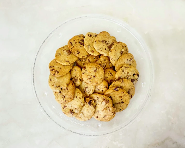 chocolate chip cookies in a clear bowl sitting on a marble counter