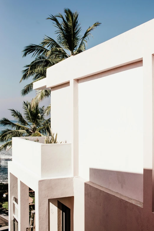 a balcony with a view of the ocean and palm trees, inspired by Ricardo Bofill, unsplash, minimalism, white and pink, bali, wall structure, exterior