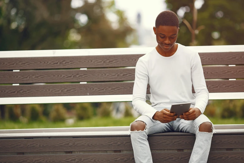 the young man is sitting on a bench and looking at his phone