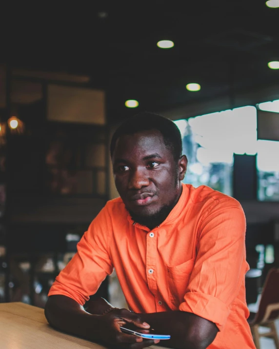 a man sitting at a table with a cell phone, pexels contest winner, happening, adut akech, wearing an orange t-shirt, standing in a restaurant, prideful look