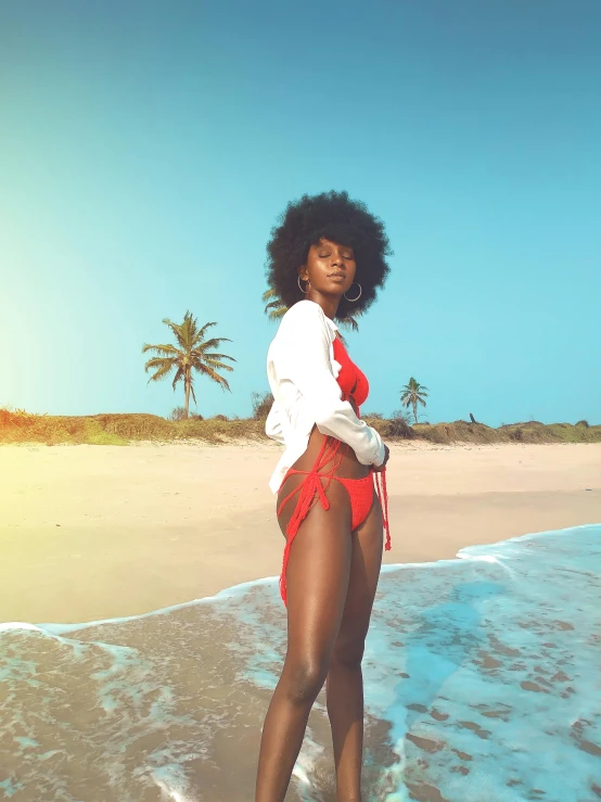 a woman standing on a beach next to the ocean, an album cover, trending on unsplash, afrofuturism, in retro swimsuit, natural hair, post processed 4k, red body suit