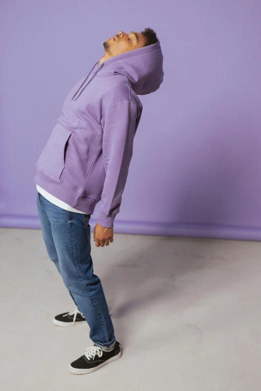 a person wearing a hooded jacket and jeans, in front of a purple backdrop