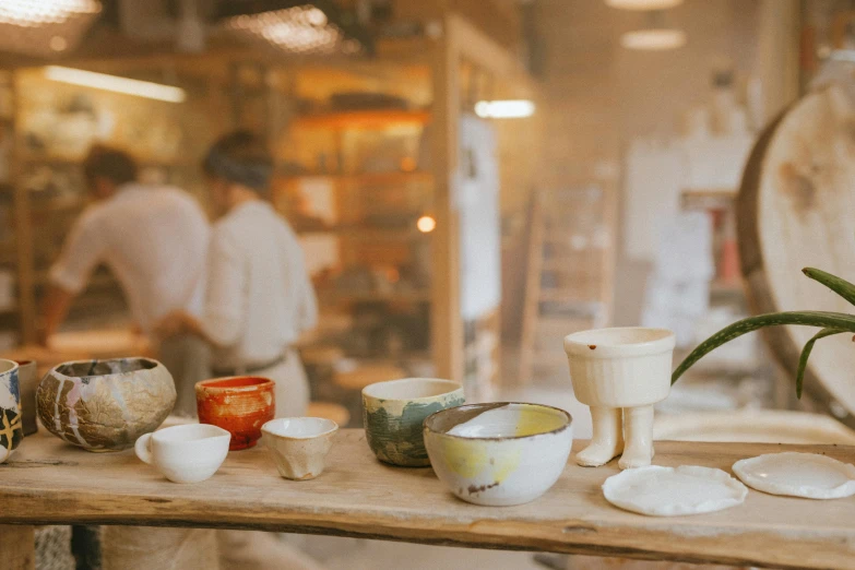 a group of bowls sitting on top of a wooden table, a still life, trending on unsplash, mingei, large jars on shelves, person in foreground, small manufacture, plaster