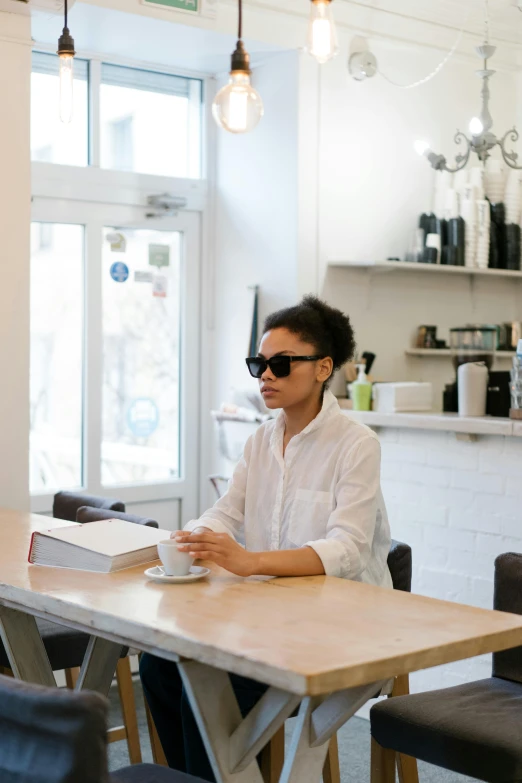 a woman sitting at a table in a coffee shop, by Nina Hamnett, wearing shades, ashteroth, white kitchen table, dwell