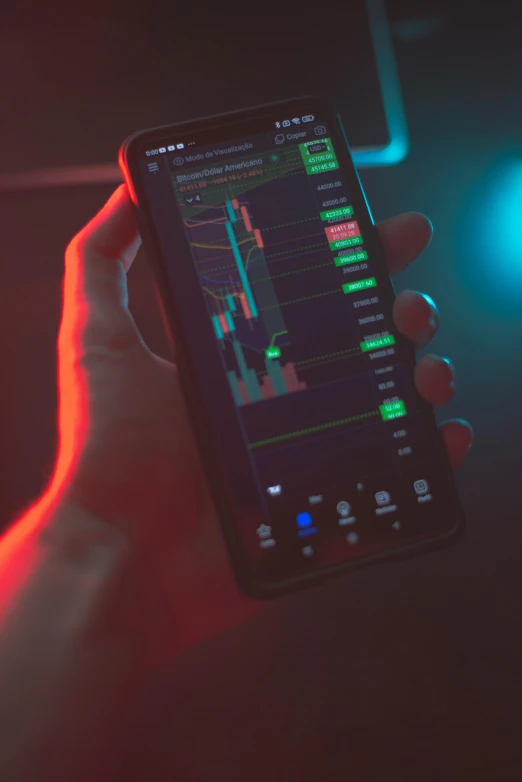 a person holding a cell phone in their hand, trending on pexels, holography, displaying stock charts, red and green lighting, edible crypto, dark themed