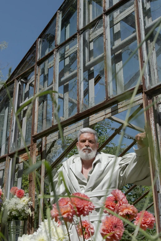 a man in a robe standing in front of a greenhouse, silver hair and beard, person made out of glass, carnation, filmstill