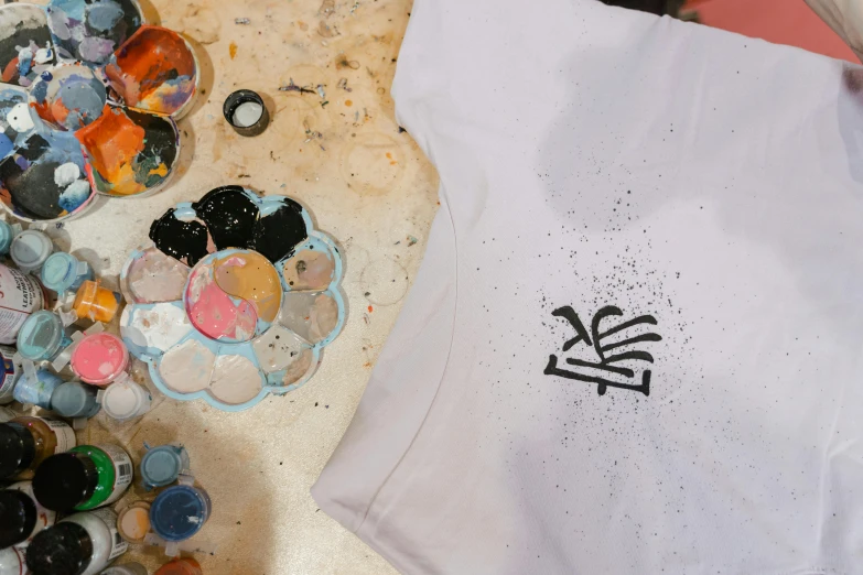 a white shirt sitting on top of a wooden table, a screenprint, inspired by Shōzō Shimamoto, unsplash, process art, spray paint, high angle close up shot, wearing a t-shirt, in a workshop