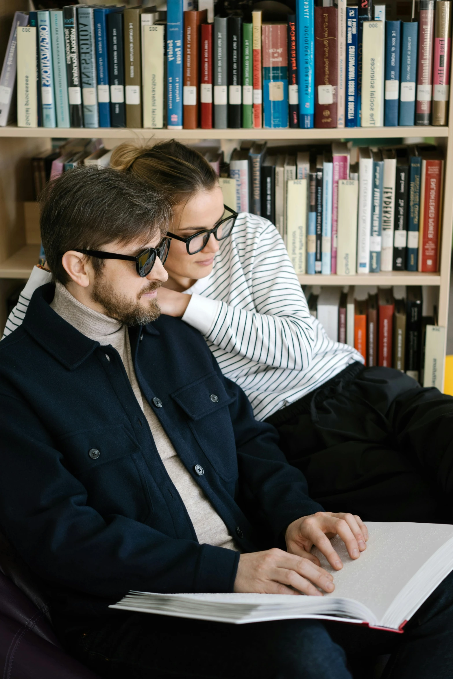 a man and a woman sitting on a couch in front of a bookshelf, trending on reddit, academic art, wearing black frame glasses, on a desk, academic clothing, concentrated