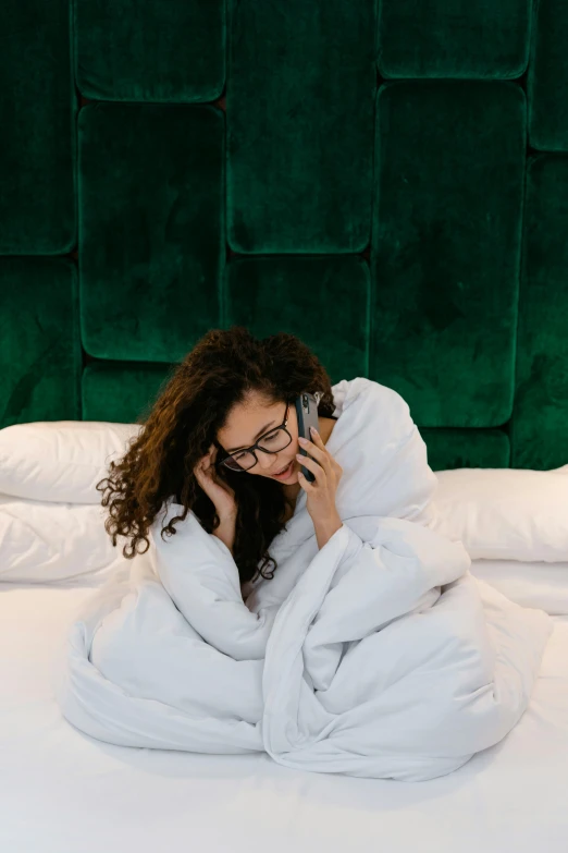 a woman laying on a bed talking on a cell phone, by Julia Pishtar, happening, green robe, girl with glasses, curled up under the covers, premium