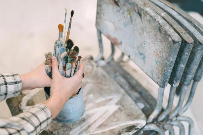 a person holding onto paintbrushes and a small cup