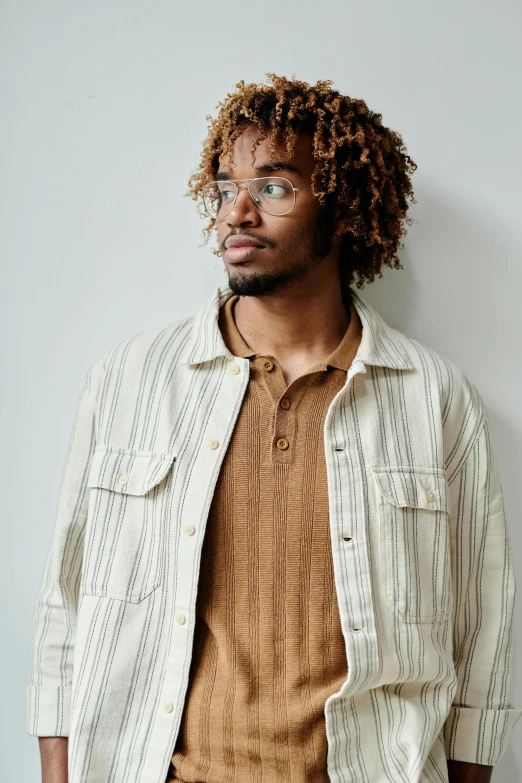 a man standing in front of a white wall, inspired by Charles Alston, trending on pexels, wear's beige shirt, amber glasses, wearing stripe shirt, east african man with curly hair