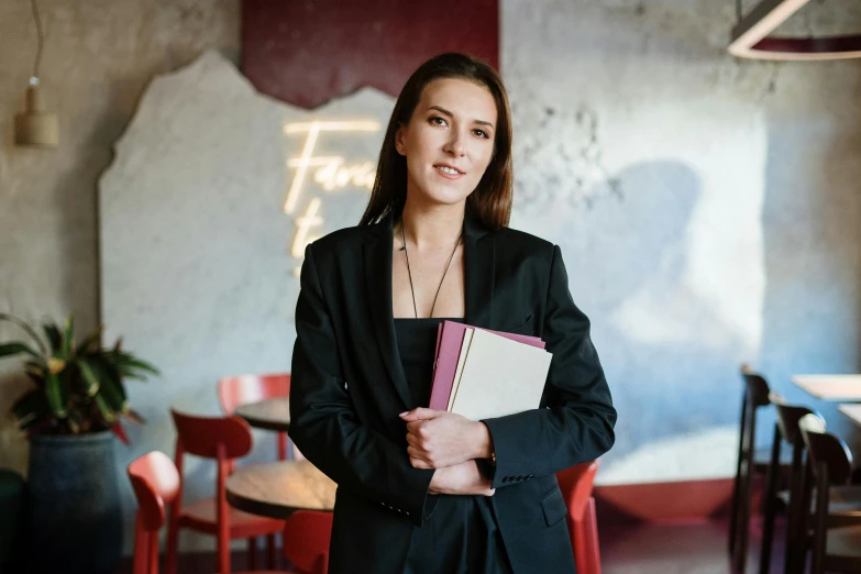 a woman standing in a restaurant holding a folder, a portrait, by Emma Andijewska, pexels contest winner, academic art, lawyer suit, 15081959 21121991 01012000 4k, holding books, young female