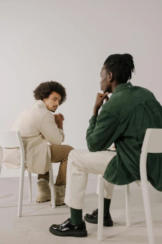 a man and a woman sitting at a table, trending on unsplash, two young men, sitting in an empty white room, brown skinned, sitting on a chair