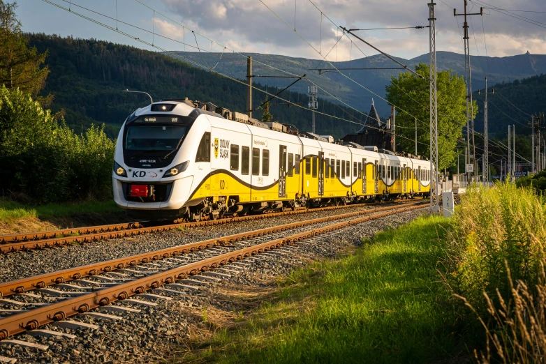 a yellow and white train traveling down train tracks, minna sundberg, summer evening, avatar image