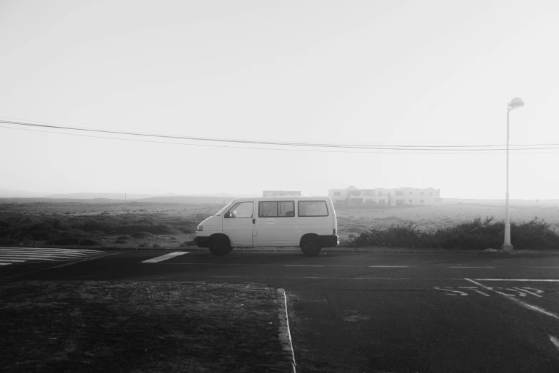 a black and white photo of a van parked in a parking lot, near the seashore, street photo