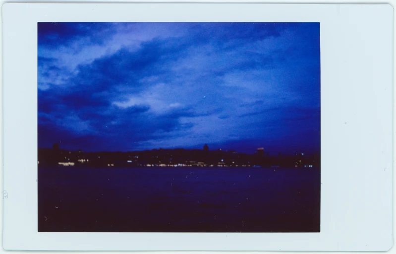 a large body of water under a cloudy sky, a polaroid photo, inspired by Thomas Struth, hurufiyya, blue lights and purple lights, ballard, in frame, phot