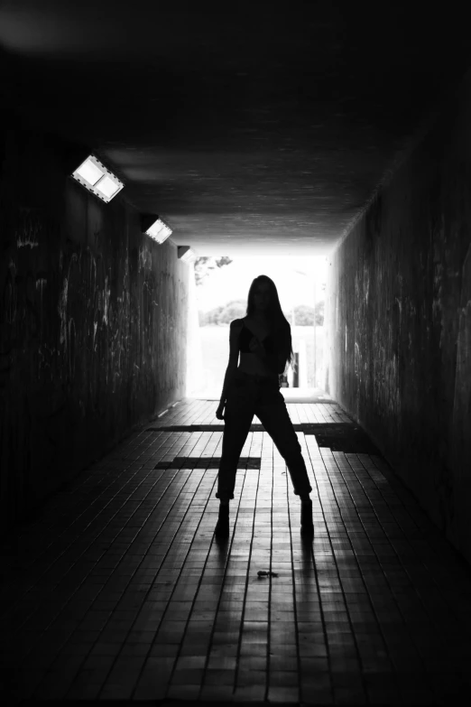 a black and white photo of a woman in a tunnel, inspired by Helmut Newton, unsplash, light and space, silhouette!!!, teenage, lights, standing