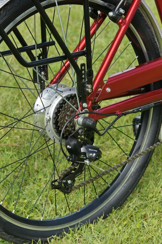 a red bike parked on top of a lush green field, exposed wiring and gears, bottom body close up, accompanying hybrid, levers