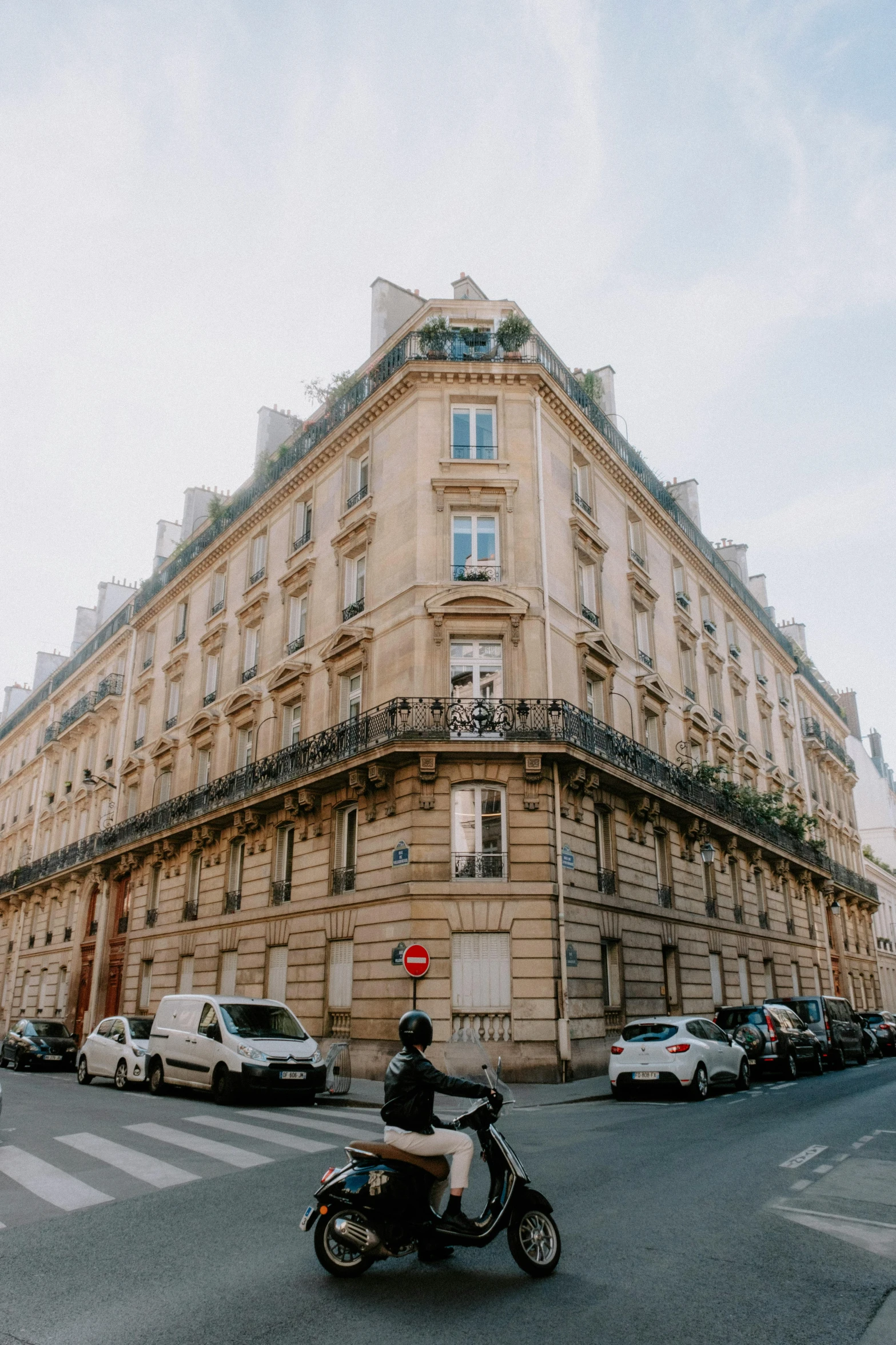 a man riding a motorcycle down a street next to a tall building, pexels contest winner, paris school, panoramic view, neoclassical architecture, old apartment, marie - gabrielle capet style