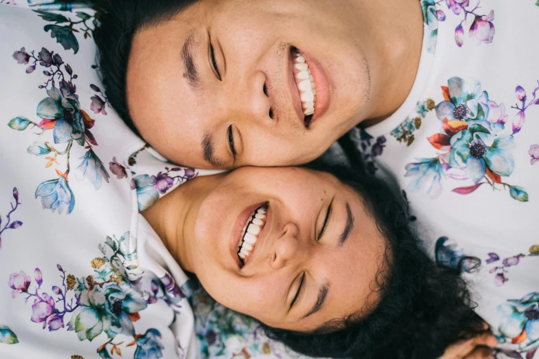 a couple laying on top of a bed next to each other, a portrait, by Carey Morris, trending on unsplash, japanese facial features, round teeth and goofy face, flowers around, adult pair of twins