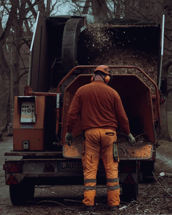 a man wearing a red coverall and an orange work uniform standing in front of a large truck