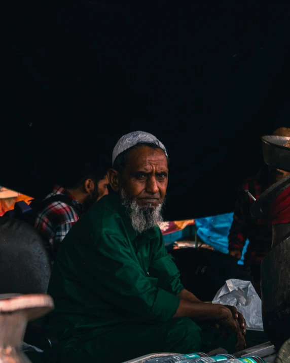 a man sitting in front of a pile of food, trending on unsplash, hurufiyya, wearing a head scarf, old dhaka, dark grey haired man, center of image