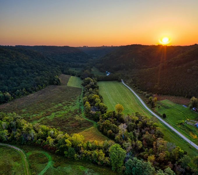 a sunset over a lush green valley near a farm