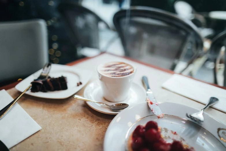 a white plate topped with a piece of cake next to a cup of coffee, pexels contest winner, happening, cafe tables, background image, jovana rikalo, aussie baristas