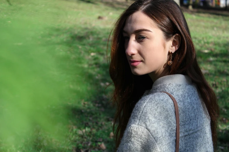 a woman that is standing in the grass, trending on pexels, earrings, wearing casual sweater, middle eastern skin, grey
