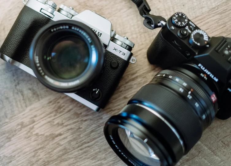 a couple of cameras sitting on top of a wooden table, by Drew Tucker, unsplash, photorealism, fujifilm x-t3, flatlay, crawling towards the camera, medium shot of two characters