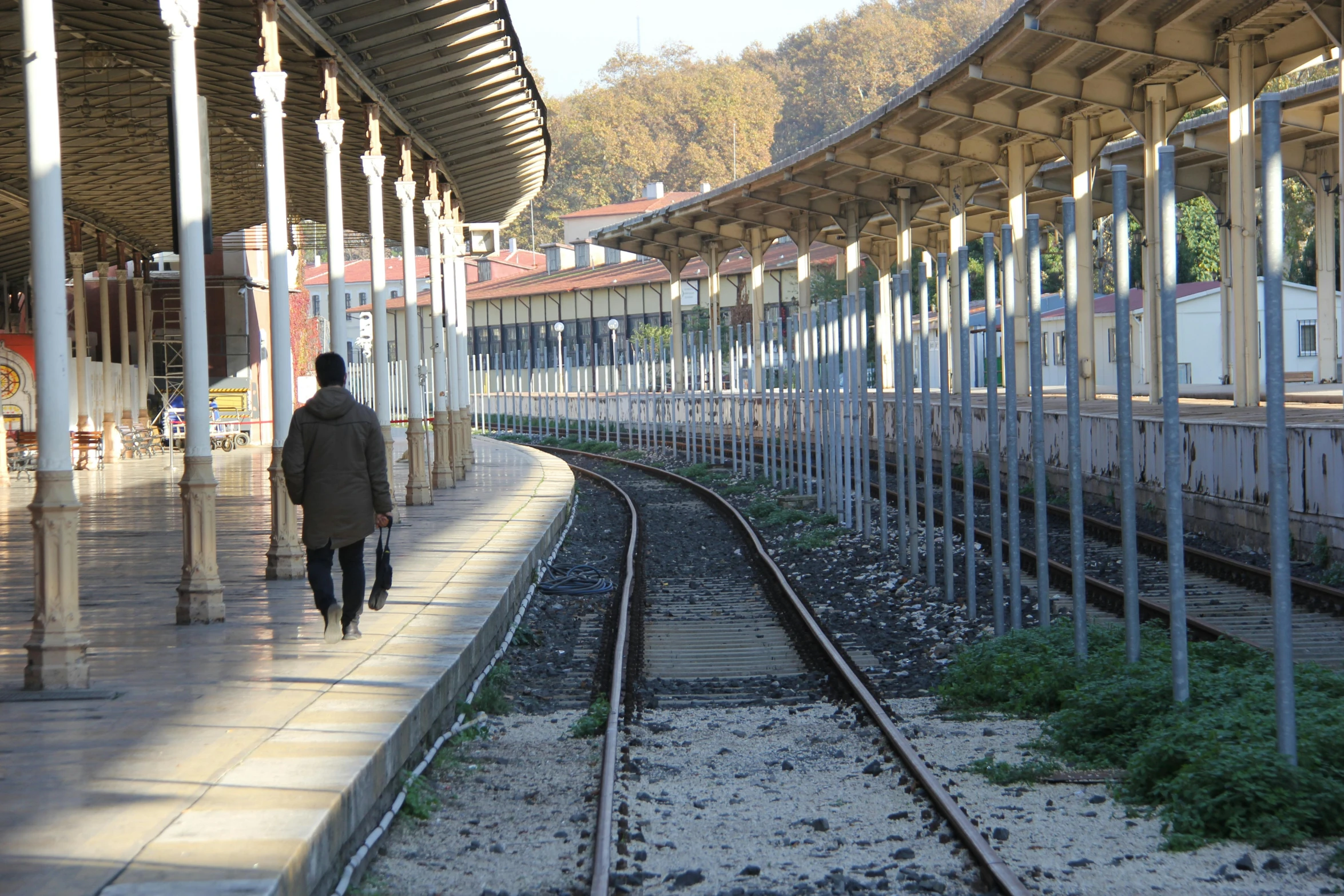 a man walking down a train track next to a train station, yan morala, edin durmisevic, university