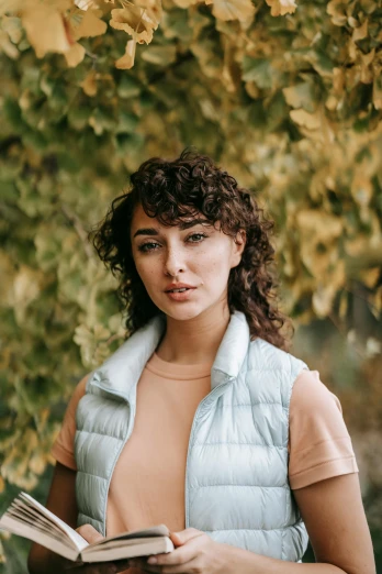 a woman reading a book under a tree, an album cover, inspired by Elsa Bleda, trending on pexels, renaissance, cropped shirt with jacket, (dark shorter curly hair), headshot portrait, wearing a vest top