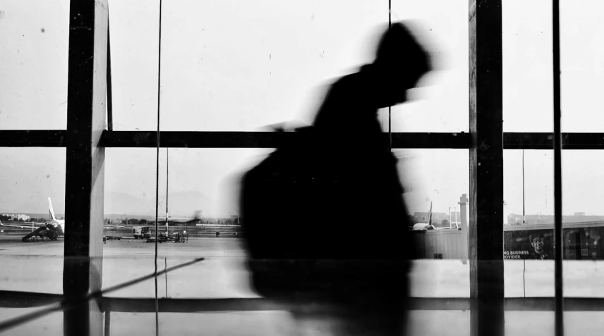 a silhouette of a person standing in front of a window, a black and white photo, at takeoff, forcing him to flee, luggage, blurry face