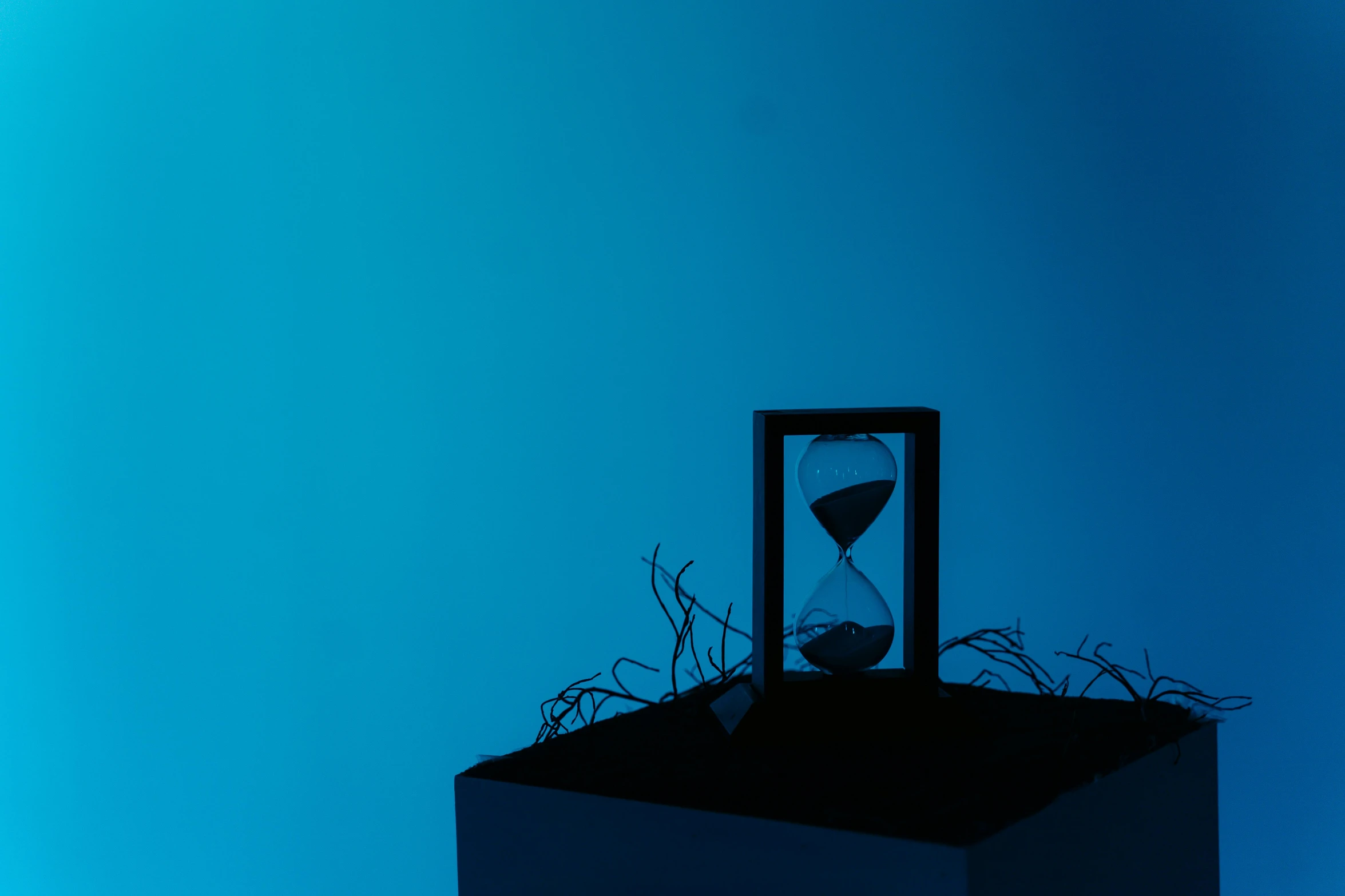 an hourglass sitting on top of a box, an album cover, inspired by Patrick Caulfield, unsplash, conceptual art, blue bioluminescent plastics, nadav kander, memory trapped in eternal time, ( ( photograph ) )