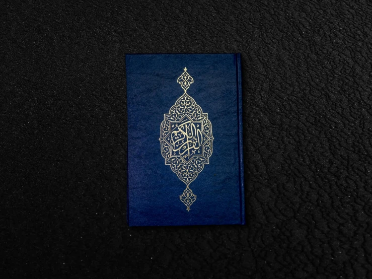 a blue book sitting on top of a black surface, by Sheikh Hamdullah, unsplash, hurufiyya, highly detailed engraving, detailed product image, front, small